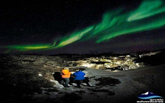 Deux personnes regardant les aurores boréales danser au-dessus de leur tête.