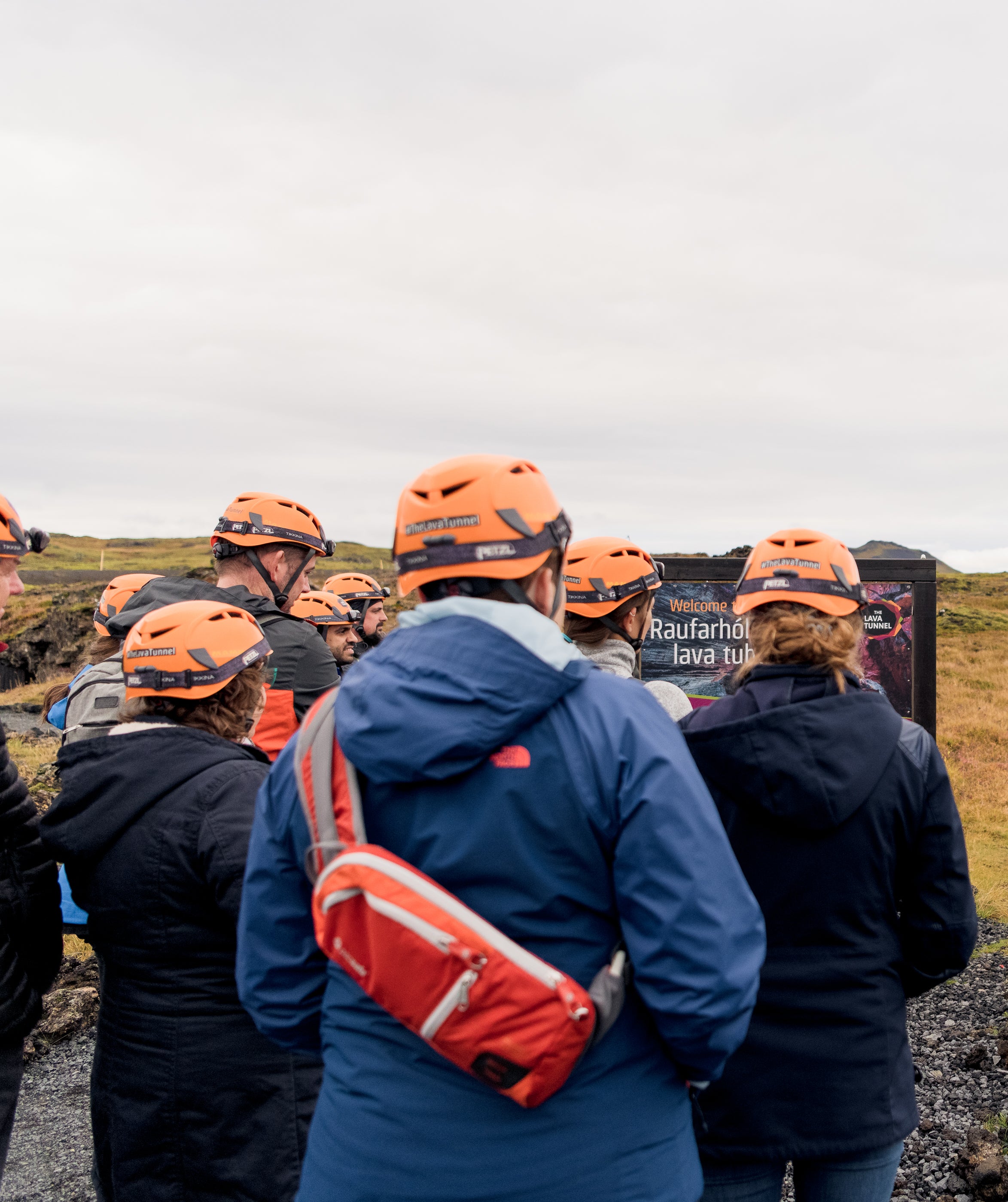 A group of people wearing helmets and waterproof clothing being briefed ahead of a lava cave tour.