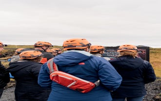 A group of people wearing helmets and waterproof clothing being briefed ahead of a lava cave tour.
