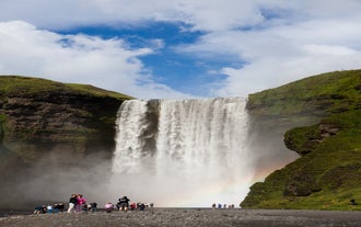 A waterfall in Iceland glimmers on a sunny day, while a rainbow shimmers near the bottom.