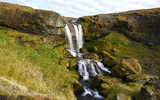 One of Iceland’s many pristine waterfalls flows between rocks amid a rugged landscape.