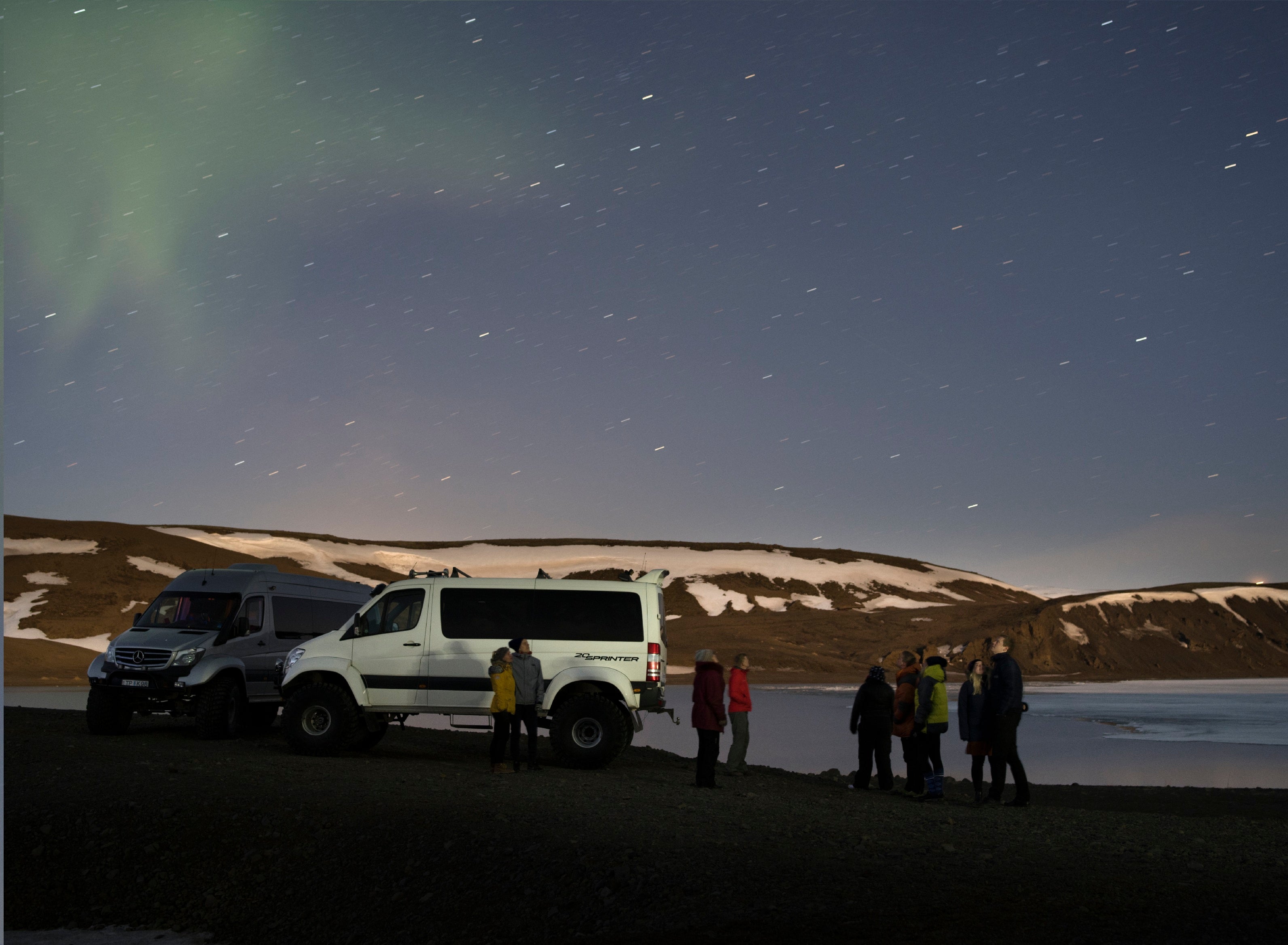 Un groupe de personnes se tenant à côté d'une super jeep alors que la nuit tombe.