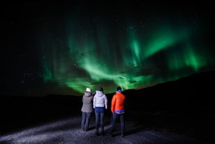 Un grupo de tres personas de pie mirando la aurora boreal en Islandia