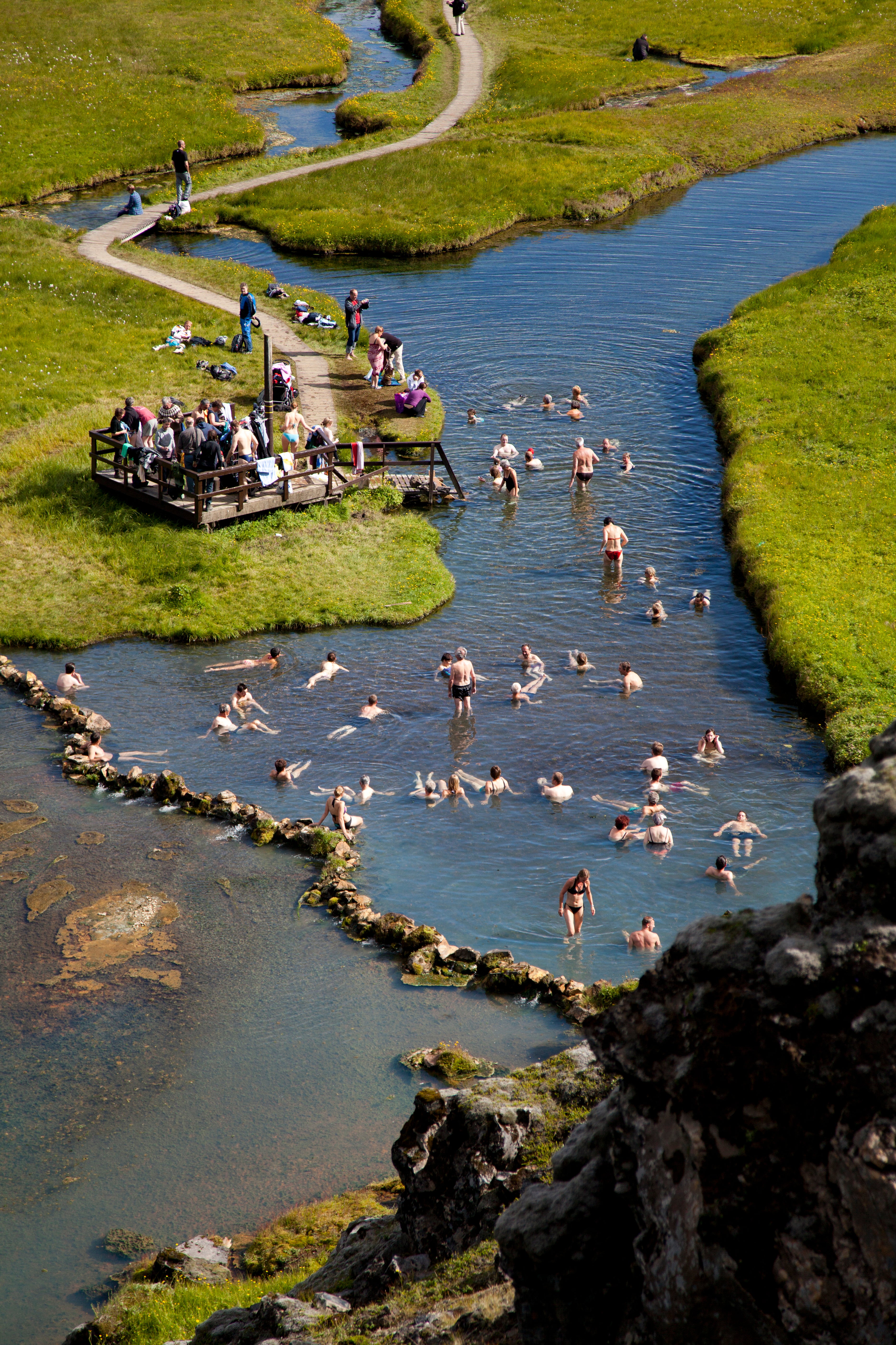 People bathe in a natural hot spring with a wooden structure and steps to enter the pool at Landmannalaugar in the Icelandic highlands.
