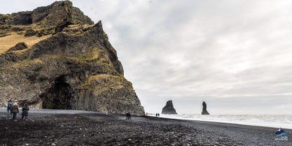 Reynisfjara black sand beach has volcanic sand, dramatic sea cliffs, and jagged sea stacks jutting from the ocean.