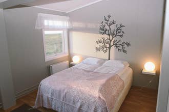 A double bed in a room at Katla Apartment with art on the wall, a bedside lamp, and a countryside view out the window.