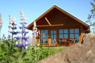 The exterior view of the wooden Family cottage in North Iceland with a table and chairs on the patio, grass surrounding, mountai