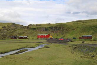 View of a cabin with a building next to it and a car park, as well as the surrounding lava field.