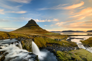 Berget Kirkjufell med vattenfallet Kirkjufellsfoss som rinner framför berget en solig dag.