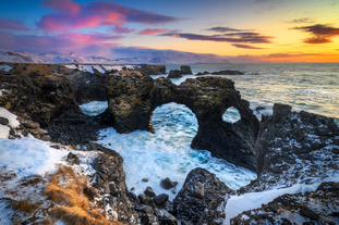 The cliffs of Londrangar seen during sunset with the ocean waves in between them.