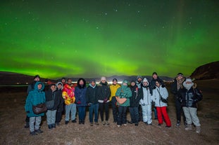 A group of lucky travelers posing for a photo while an excellent display of the aurora borealis shines in the background.