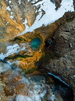 A geothermal crater seen from above with green and yellow moss and snow patches.