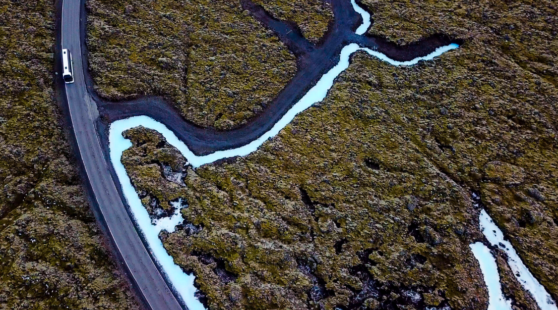 The lava fields in Iceland with a bus driving through them.