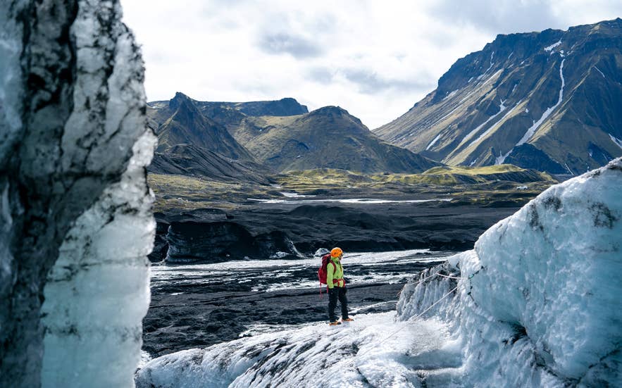 Traveler standing between glacier ice walls on Myrdalsjokull with mountains behind. Traveler standing between glacier ice walls on Myrdalsjokull with mountains behind.