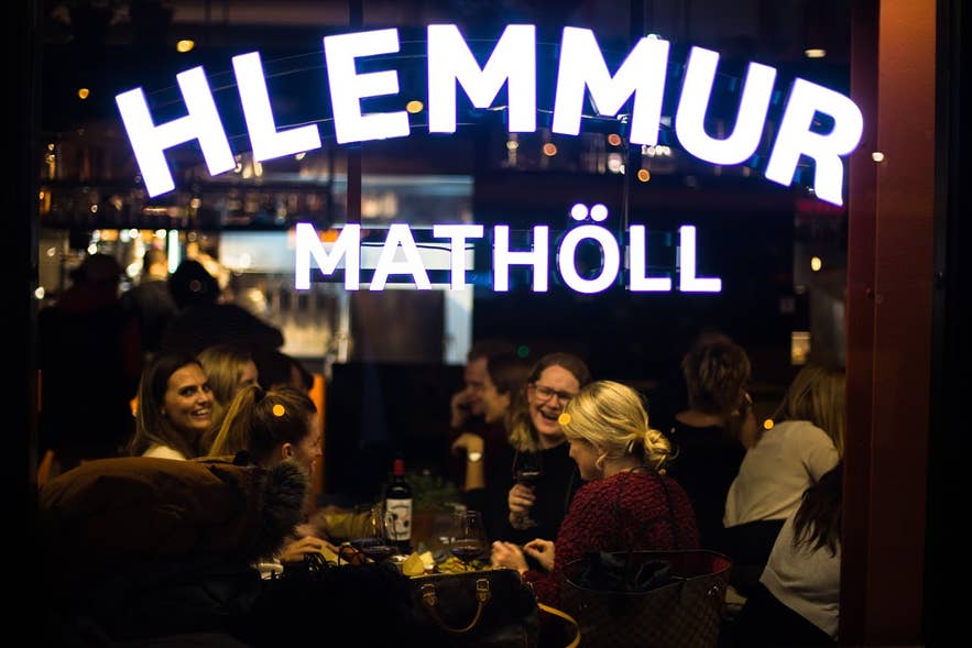Interni del mercato gastronomico Hlemmur Matholl a Reykjavík, Islanda, con persone che mangiano, bevono e socializzano sotto insegne al neon durante la sera.