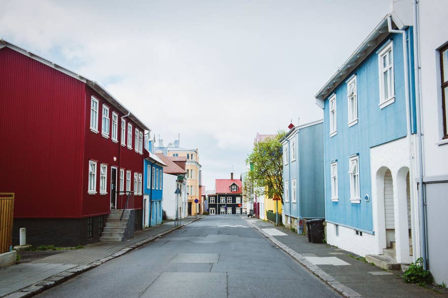 Eine Straße im Thingholtin-Viertel in Reykjavik, Island, mit bunten Holzhäusern, schmalen Wohnstraßen, roten und blauen Fassaden und einem bewölkten Frühlingshimmel.