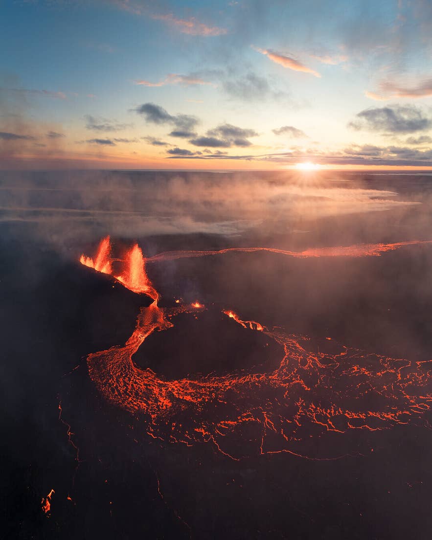 Uitbarsting bij de Sundhnukagigar-vulkaan op het Reykjanes-schiereiland met gloeiende lavastromen en rook onder een dramatische zonsondergang.