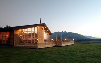 Outside view of Eyjar Fishing Lodge showing the large windows, with a towering mountain in the background.