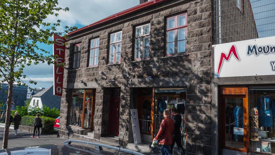 Außenansicht des Stella-Modegeschäfts in Reykjavik, Island, in einem historischen Steingebäude mit großen Schaufenstern und einem roten, vertikalen Vintage-Schild.