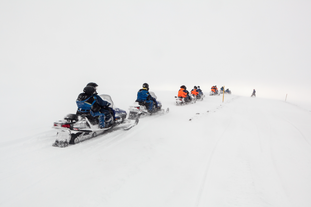 A group of people snowmobiling on a glacier.