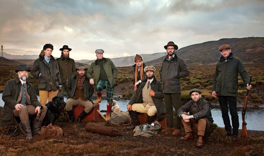 Groep mannen in klassieke outdoor kleding van Herrafataverzlun Kormaks og Skjaldar, poserend in de IJslandse hooglanden met traditionele jachtkleding, tweed petten, gewaxte jassen en vintage accessoires.