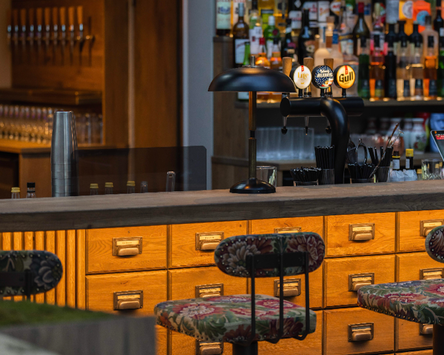 Small bar counter in Reykjavik with bottles displayed, customers seated on high stools tasting drinks and food.