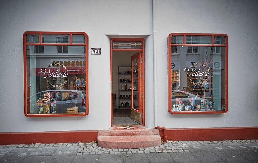 Exterior of Vínberið candy store in Reykjavik, Iceland, with a vintage-style red and white facade, large display windows filled with sweets and gift boxes, and a welcoming open doorway at number 43.