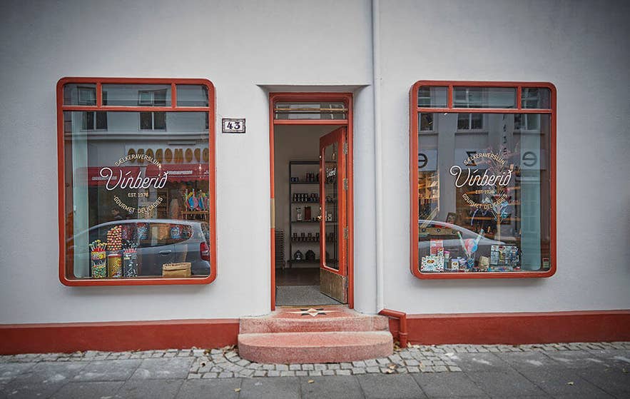 Udsiden af slikbutikken Vínberið i Reykjavik, Island, med en rød og hvid facade i vintage-stil, store udstillingsvinduer fyldt med slik og gaveæsker samt en indbydende åben døråbning ved nummer 43.