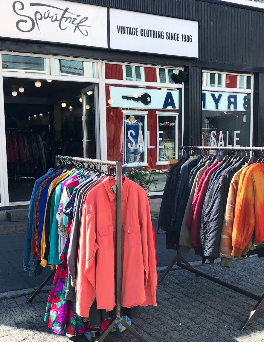 Udsiden af vintagebutikken Spuutnik i Reykjavik, Island, hvor farverige retro-tøjstykker er udstillet på stativer udenfor under et skilt med teksten "Vintage Clothing Since 1986".