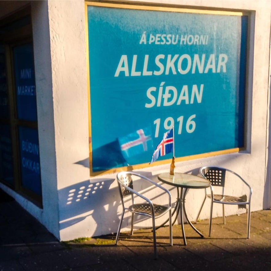 Outdoor seating beside Blahornid, a historic corner store in Reykjavik, Iceland, with a blue window sign reading “Allskonar síðan 1916” and small Icelandic flags reflecting local heritage.