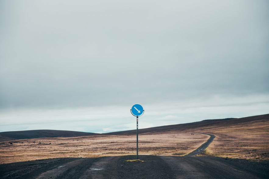 A round blue sign with a white arrow tells you to drive to the right because of a blind hill