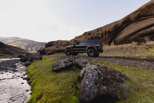 A black super jeep is seen driving close to a river in the Icelandic Highlands.