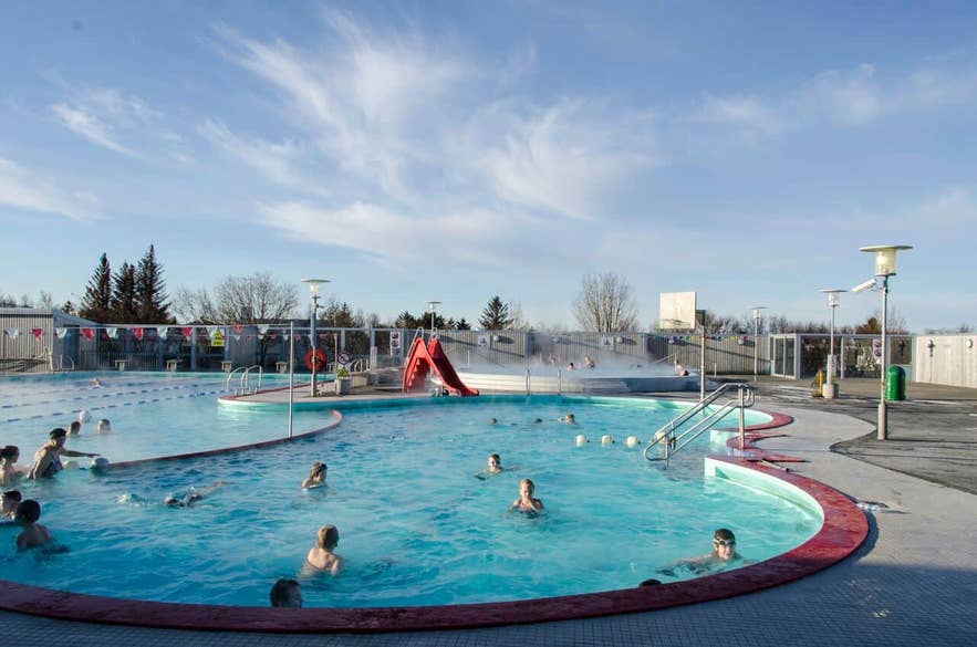 Unter strahlend blauem Himmel genießen Menschen das Außenbecken des Vesturbaejarlaug, eines der beliebtesten Schwimmbäder in Reykjavik.