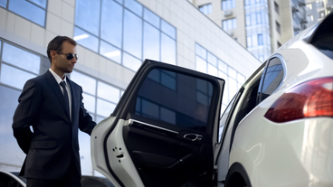 A driver wears sunglasses as he opens the door to a white vehicle.