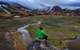A traveler sits on a rock formation while exploring Landmannalaugar in the Icelandic Highlands.