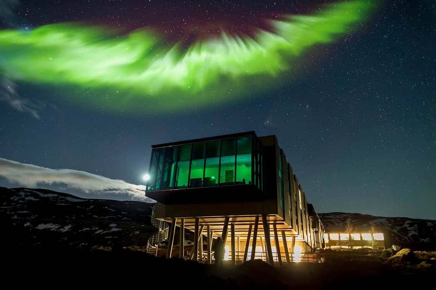 ION Adventure Hotel in Thingvellir with northern lights above, modern glass building under vivid green aurora in Iceland