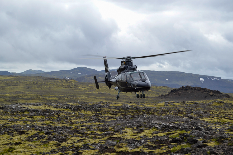 Helicopter flying close to a moss covered field.