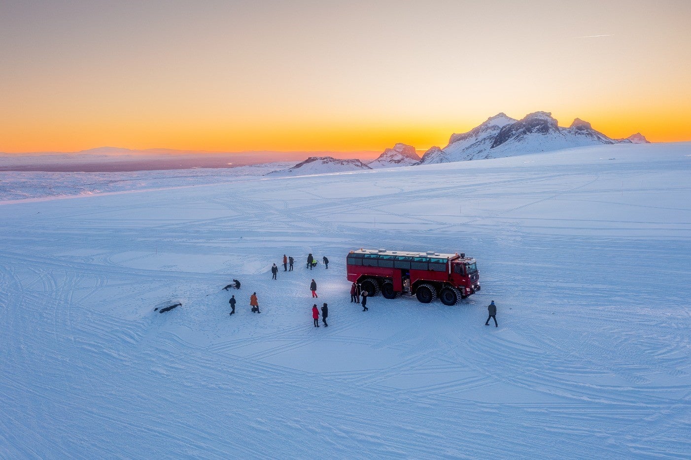 Un groupe de personnes et un camion rouge vus au coucher du soleil au sommet d'un glacier.