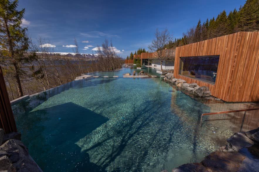 Das Haupt-Geothermalbecken der Forest Lagoon mit dem Spa-Gebäude aus Holz und Bergen im Hintergrund