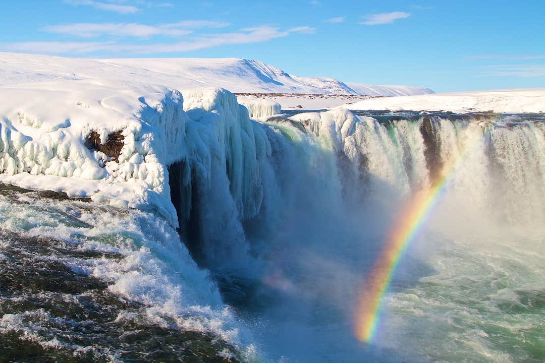 Un arc-en-ciel apparaît dans la brume au-dessus de la cascade de Godafoss et de ses environs enneigés en hiver en Islande.