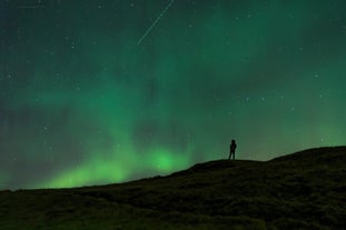 A traveler photographed on a mountain pass with the aurora borealis in the background.