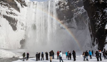 People stand in front of Skogafoss waterfall admiring the rainbow.