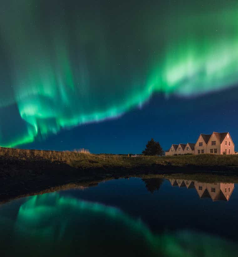 The northern lights seen dancing above a lake and a white house in Iceland.