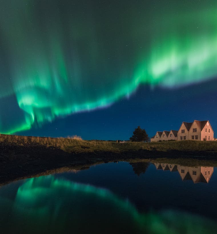 The northern lights seen dancing above a lake and a white house in Iceland.