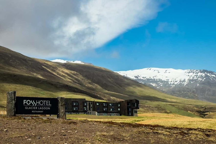 Fosshotel Glacier Lagoon set against green hills and snow-capped mountains in Southeast Iceland, located near Jokulsarlon Glacier Lagoon and offering modern accommodation in a remote natural setting.