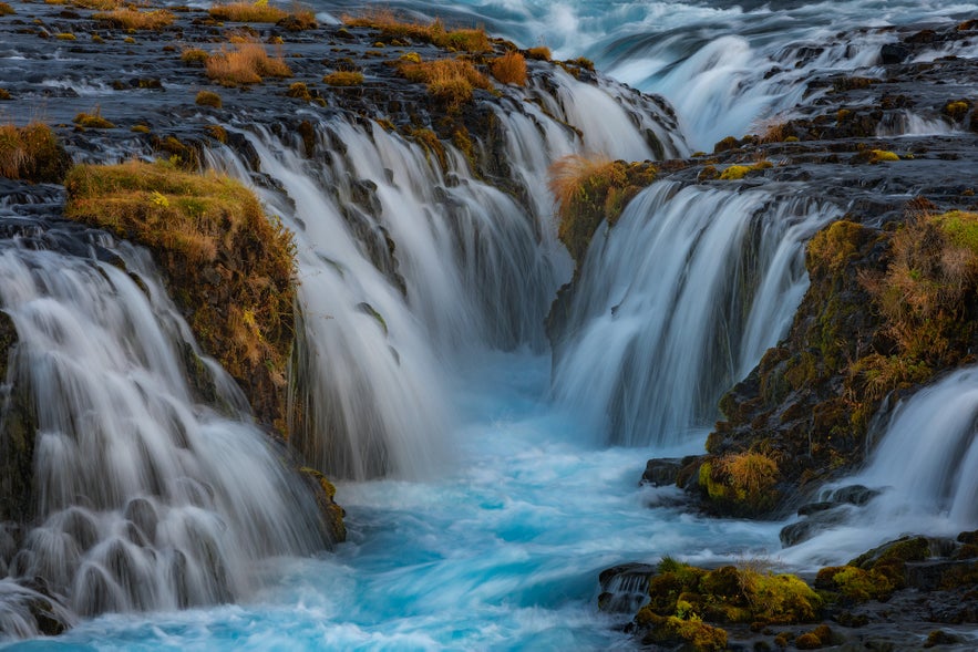 Close-up of the vivid blue water rushing through the dark basalt channels of Bruarfoss waterfall in Iceland.