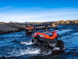 People driving red buggies cross a river in Iceland.