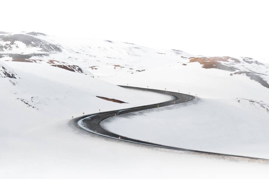 Snow-covered road curving through white hills in Iceland, where black ice forms near freezing temperatures.