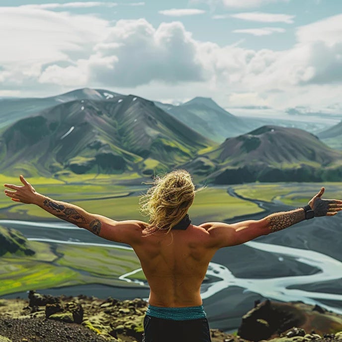 A man with no shirt on spreads his arms wide in front of some spectacular Icelandic scenery.