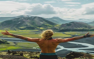 A man with no shirt on spreads his arms wide in front of some spectacular Icelandic scenery.